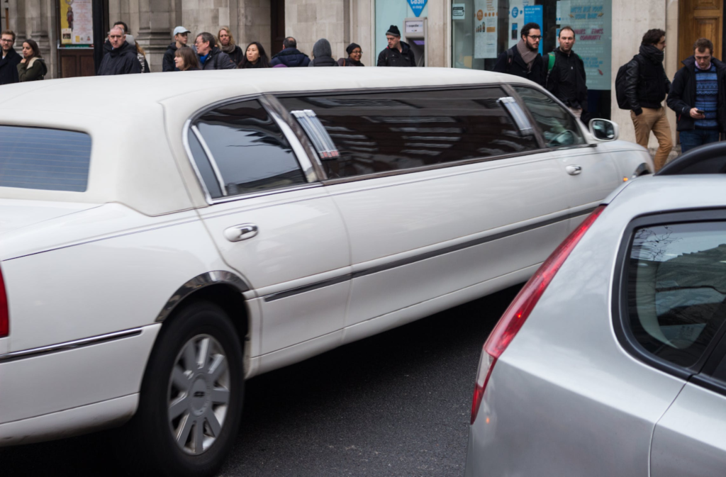 A white limousine in parked in front of a bunch of people